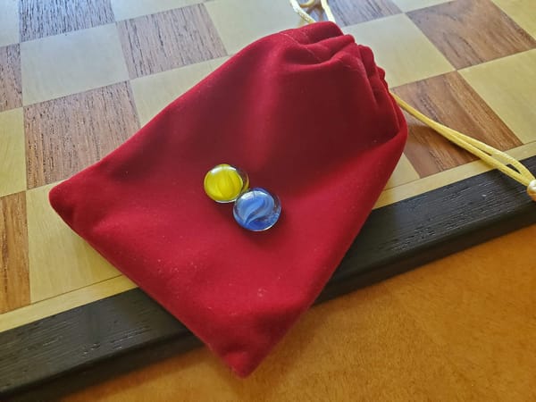 Two marbles, one yellow and one blue, resting atop a red satin bag.